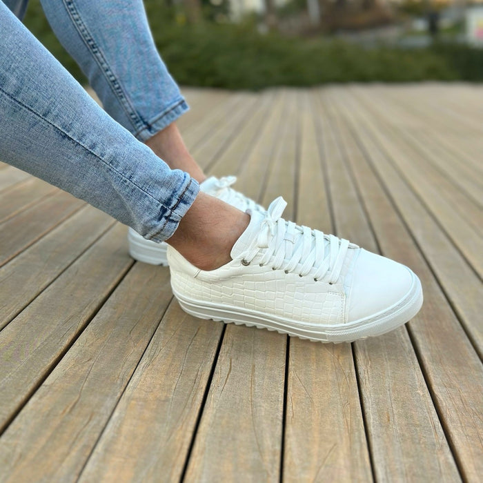Martin Valen Dino low-top white sneakers worn, side view showing croc-textured upper, tied laces and thick ridged sole on wooden deck