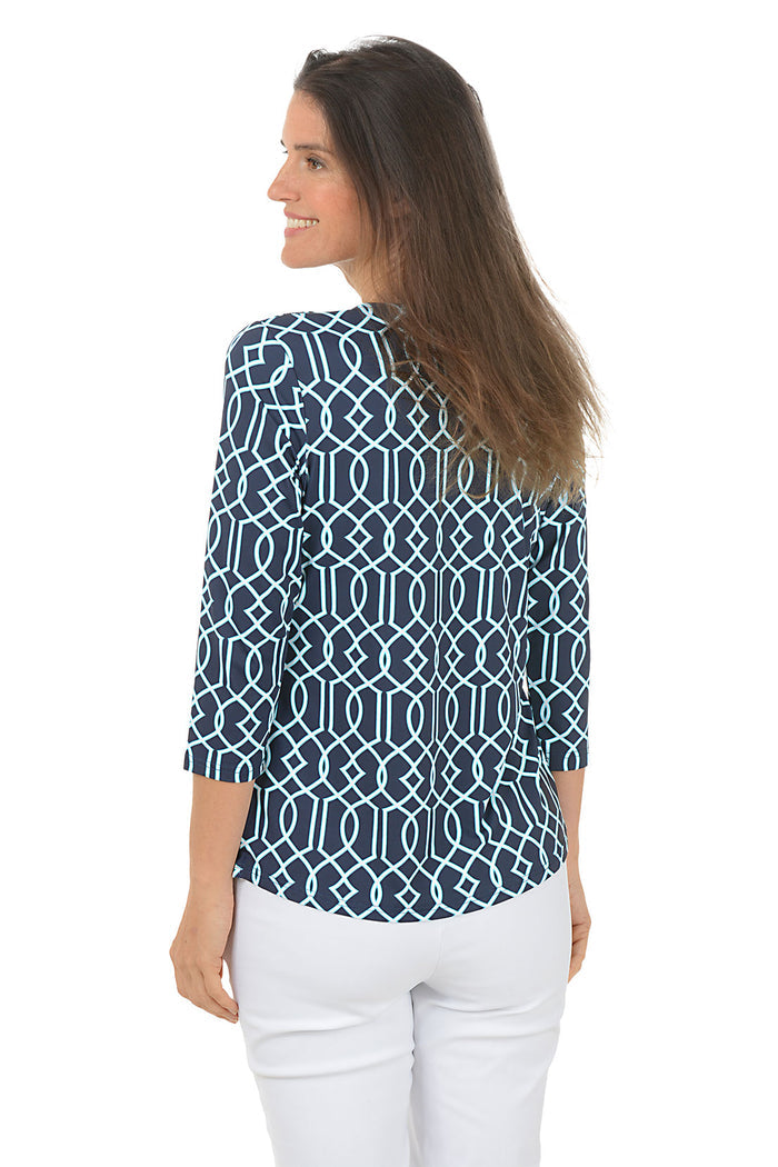 Woman wearing a blue patterned top and white pants on a white background. Back shot.