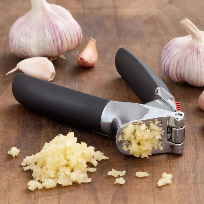 Garlic press with minced garlic on a wooden surface with whole garlic cloves.
