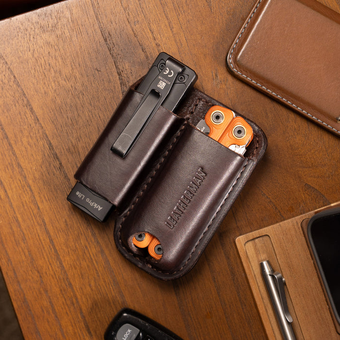Brown leather sheath holding a black flashlight and orange multitool on a wooden desk