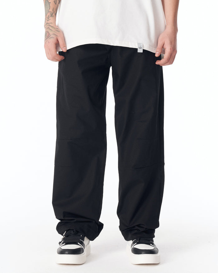 Martin Valen black wide-leg trousers, mid-thigh front view showing adjustable cuff and white brand tag