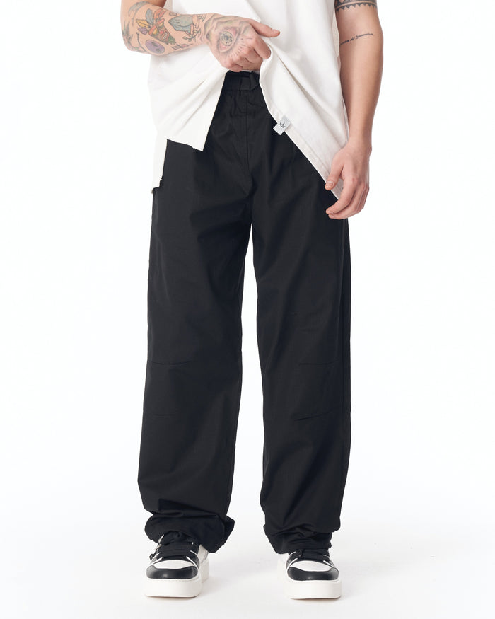 Martin Valen black wide-leg trousers, full front view showing cinched adjustable cuff at ankle and black-white sneakers