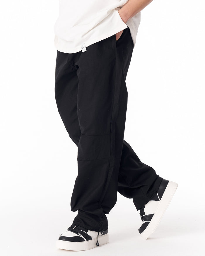 Martin Valen black wide-leg trousers with adjustable cuff, three-quarter front view showing walking motion