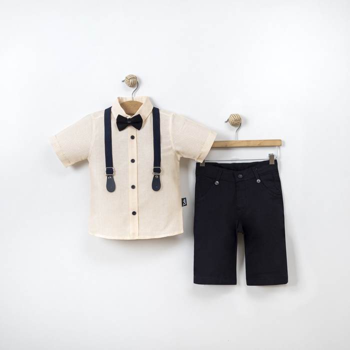 Boys formal outfit displayed on hangers, featuring a beige short-sleeve shirt with suspenders and bow tie, paired with black shorts.