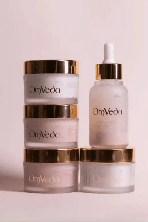 OmVeda skincare set with jars and serum bottle with dropper, in gold and clear glass