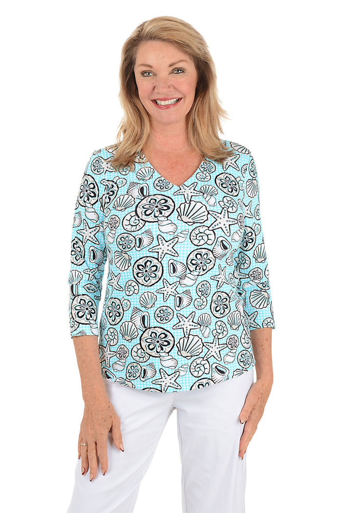 Woman wearing a blue top with shell pattern on a white background.