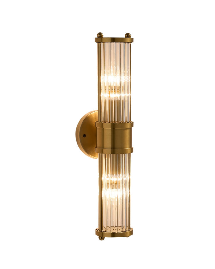 Brimsley II Wall Sconce illuminated, featuring a vertical brass body with ripple-textured clear glass panels, shown on a white background highlighting its elegant glow and elongated form.