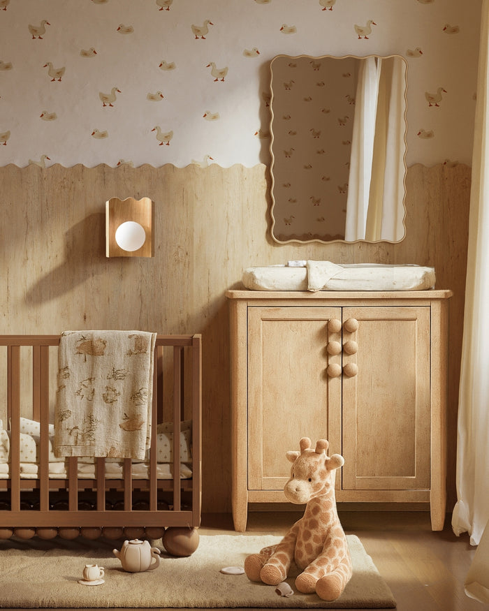 Nursery interior with an oak wood wall sconce featuring a round white glass globe, mounted above a wooden crib and changing cabinet.