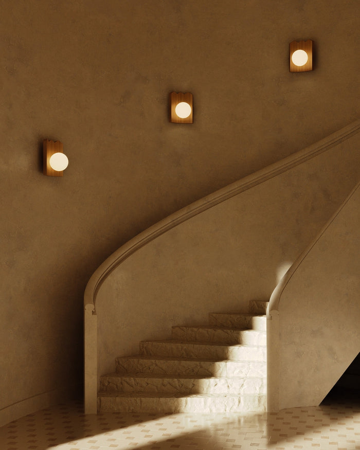 Clemence oak wood wall sconces with white glass globes installed along a curved staircase wall, emitting warm ambient light.