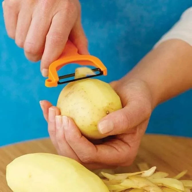 Person peeling a potato with an orange European style peeler against a blue background