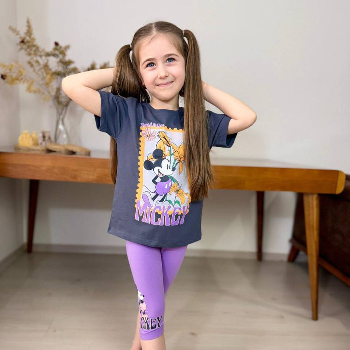 Smiling girl in a navy blue Mickey Mouse T-shirt with a floral graphic, paired with purple capri leggings featuring a matching Mickey print.