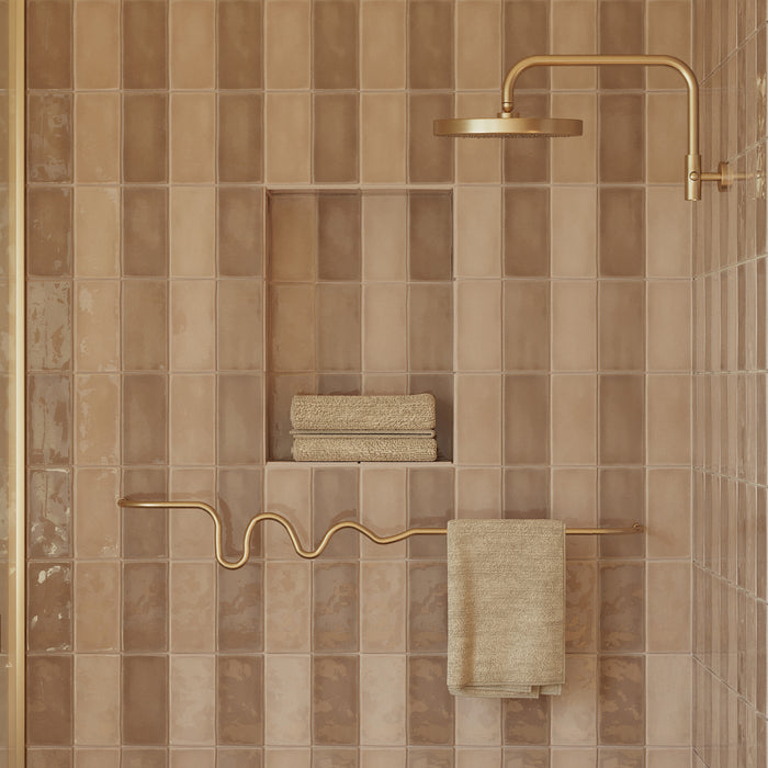Brass wavy towel bar mounted on a tiled shower wall, holding a folded towel beneath a brass shower fixture.