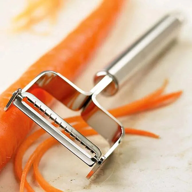 A stainless steel julienne peeler with a long handle and a two-bladed end peeling carrots.