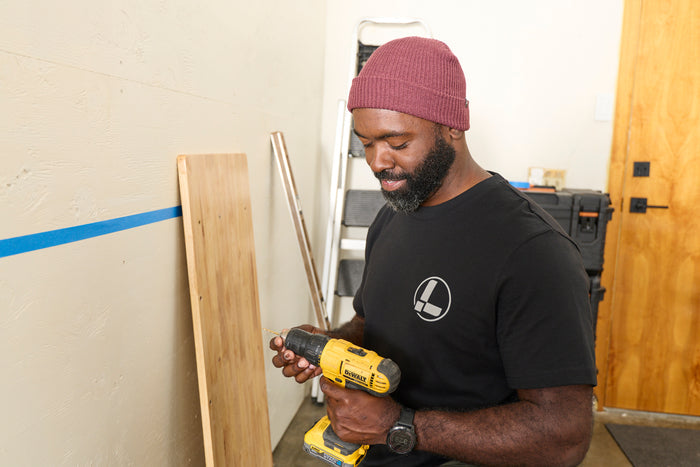 A person wearing a black Leatherman Classic Tee holding a yellow power drill while working indoors.