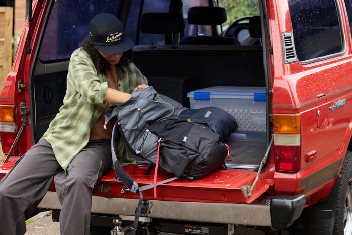 A woman wearing a black Leatherman Vintage 5 Panel Hat packing a backpack on the open tailgate of a red vehicle.
