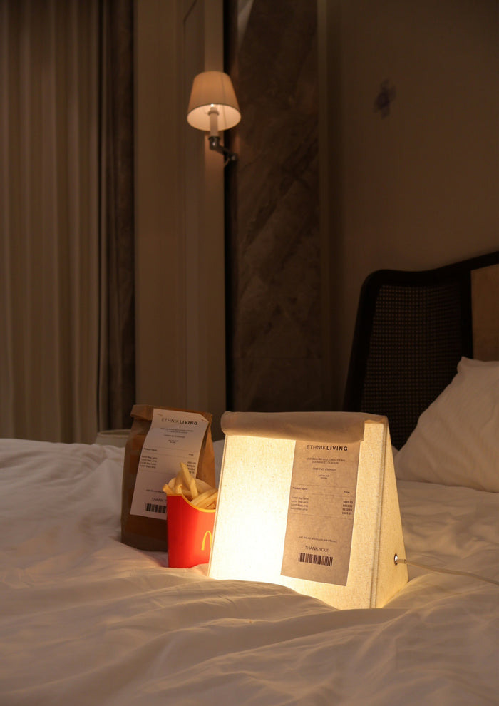 Glowing fabric lamp on a bed beside a takeout bag and fries.