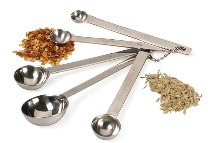 Set of stainless steel measuring spoons with spices on a white background