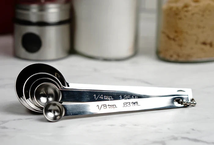 Set of metal measuring spoons on a marble surface with jars in the background