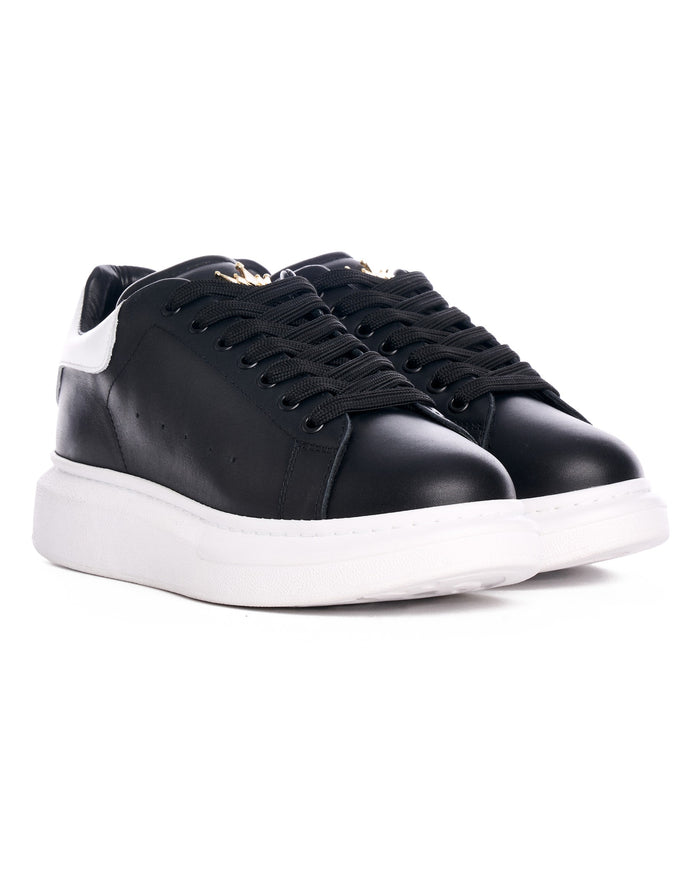 Pair of Martin Valen Crowned Hype Sole black sneakers, close-up on laces and small gold crown emblem on the tongue
