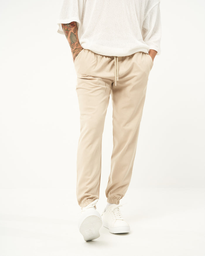 Martin Valen men's beige elastic-waist loose jogger, mid-body view showing drawstring and hand in pocket