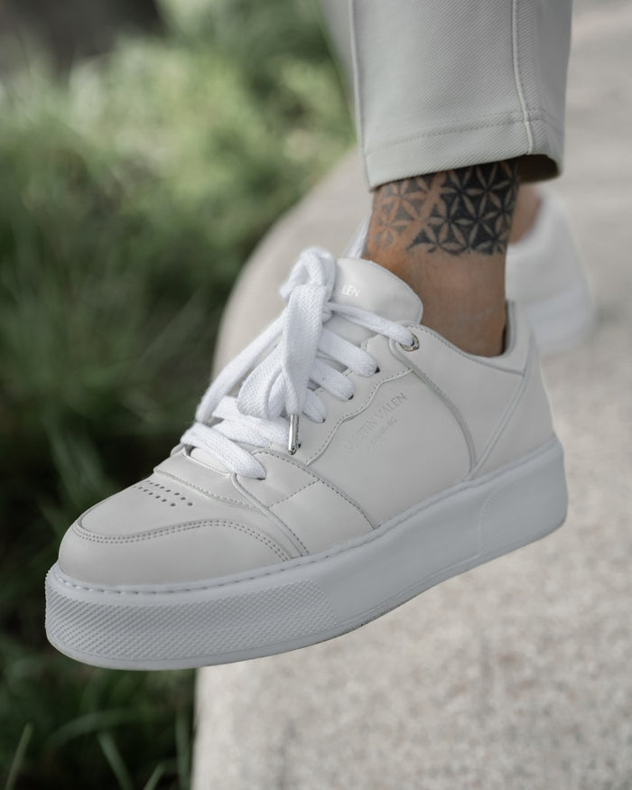 Martin Valen men's high sneakers in white, outdoor side close-up worn on foot beside greenery showing embossed logo and perforated toe