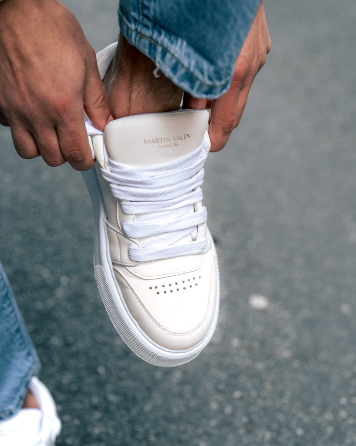 Martin Valen white men's high-top sneakers worn outdoors, top close-up as hands adjust the laces and tongue logo