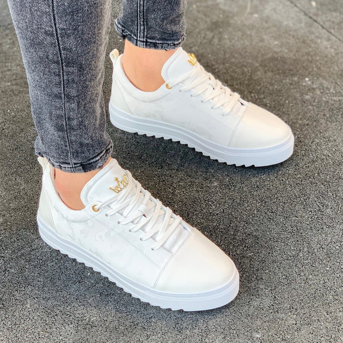 Martin Valen white low-top sneakers worn on feet, three-quarter view showing ridged sole, subtle camo side pattern and gold crown detail