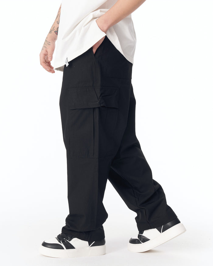 Martin Valen relaxed black cargo pants, mid-front view showing side pockets and model with hands in pockets