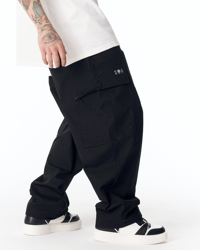 Martin Valen men's black relaxed cargo pants, side view showing flap cargo pocket and white sneaker detail