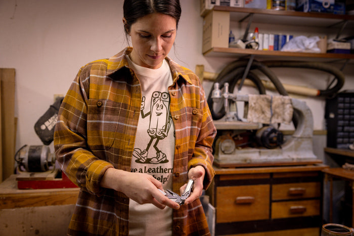 A person wearing a natural-colored Leatherman Mr. Wave Tee with a cartoon multitool design opening a Leatherman multitool in a garage.