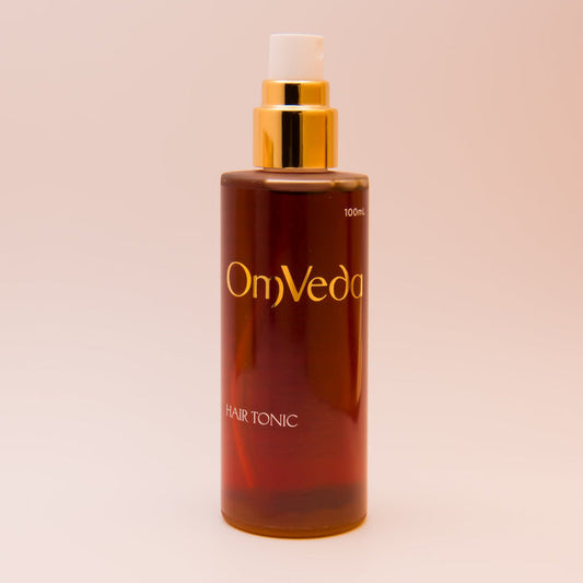 OmVeda hair tonic bottle with gold pump, amber formula, 100 ml