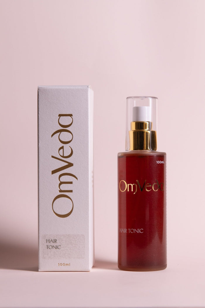 OmVeda hair tonic bottle and box, amber liquid with gold pump, 100 ml