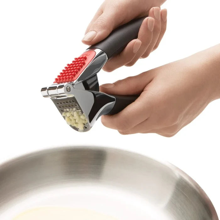 Hand using a garlic press to crush garlic over a frying pan on a white background