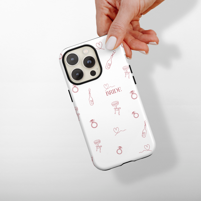 Blush pink tough phone case with wedding-themed designs and BRIDE text, held in a hand.