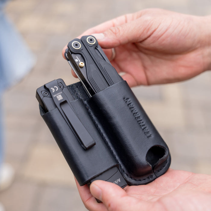 Hands holding a black leather sheath carrying two black multitools outdoors
