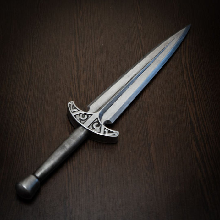Decorative dagger with a silver blade and black handle on a dark wooden surface