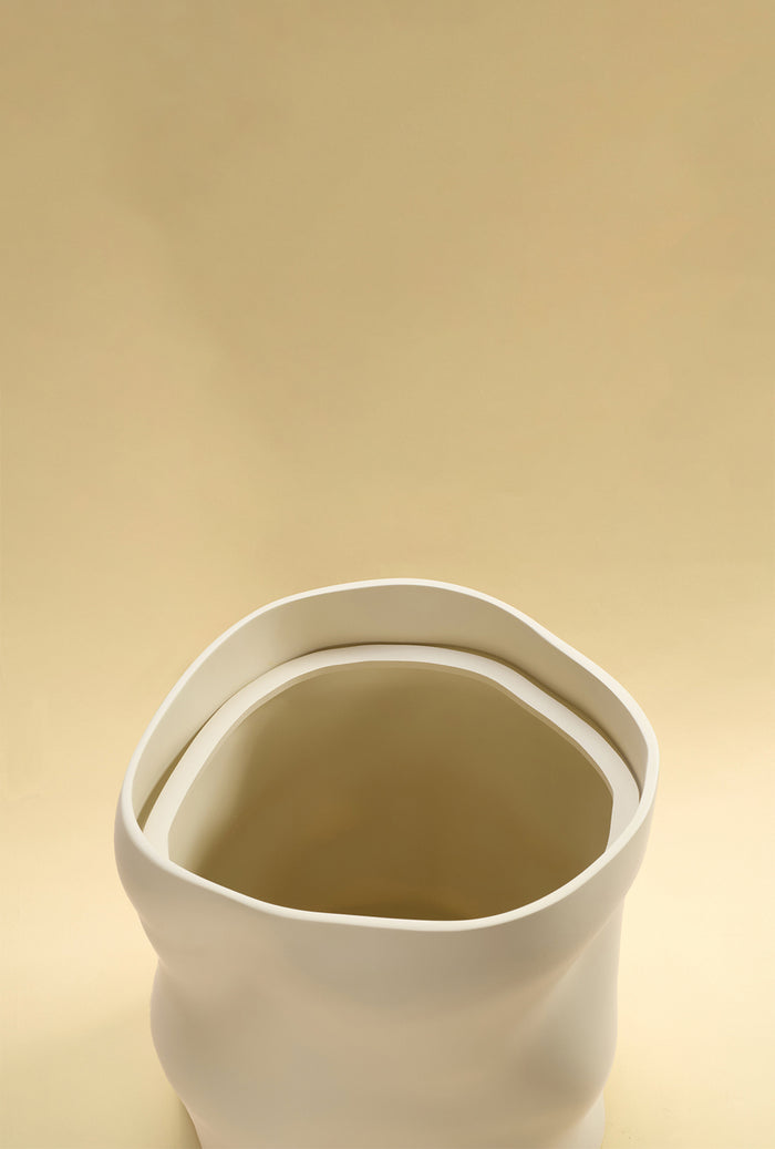 An open beige sculptural dustbin shown from above, highlighting the rounded rim and interior, against a light yellow background.