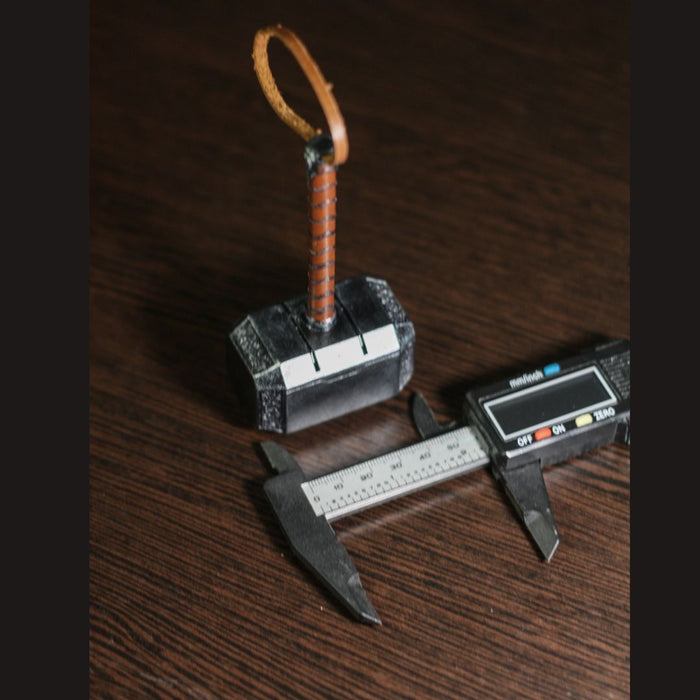 Thor Hammer miniature 1:4 scale replica with leather strap and caliper measuring its size on wooden surface