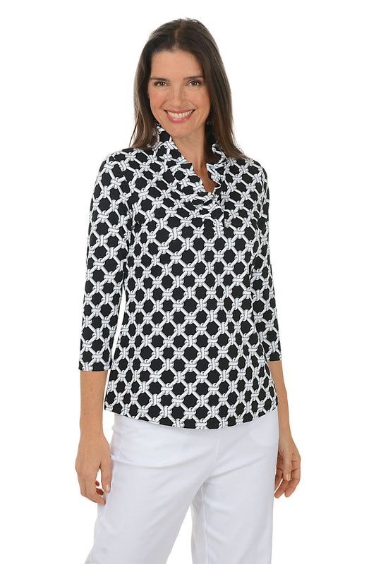 Woman wearing a black and white patterned blouse with white pants on a white background.