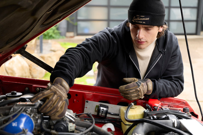 A person wearing a black Leatherman Vintage Beanie working under the hood of a red vehicle.