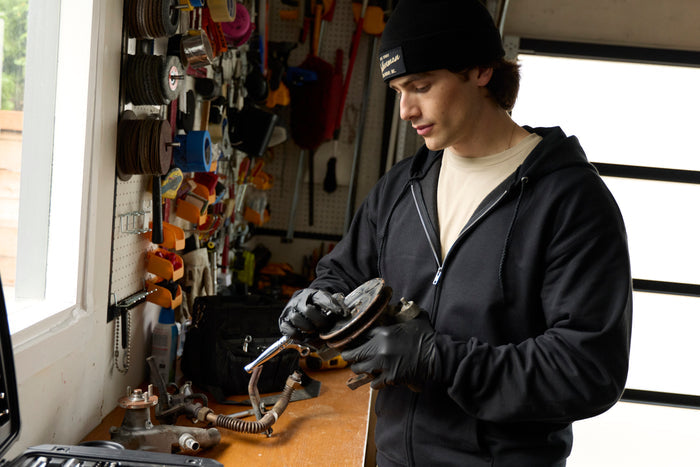A person wearing a black Leatherman Vintage Beanie working on a car part in a garage.