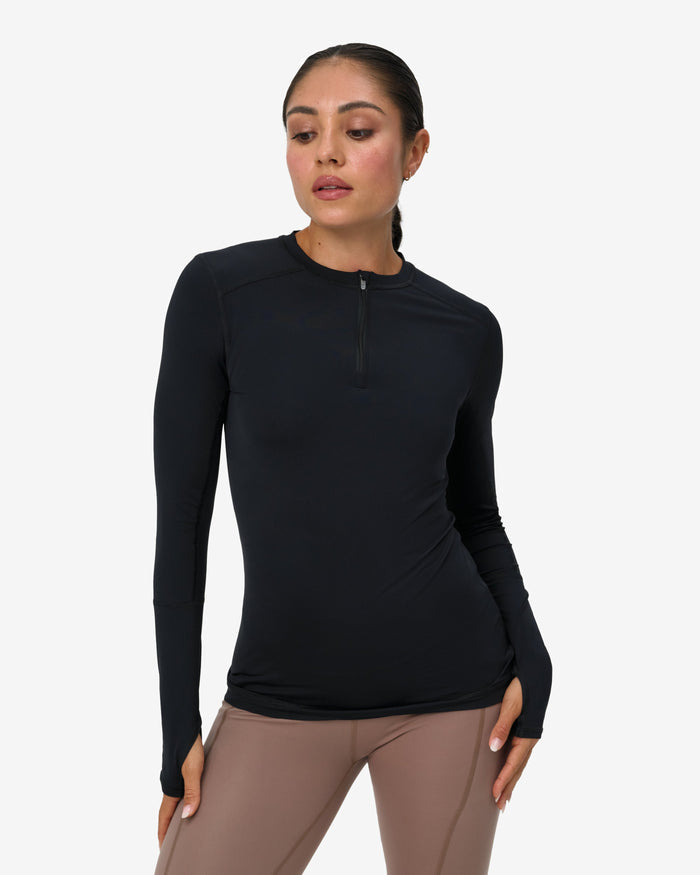 Woman wearing a black long-sleeve top and brown pants on a white background