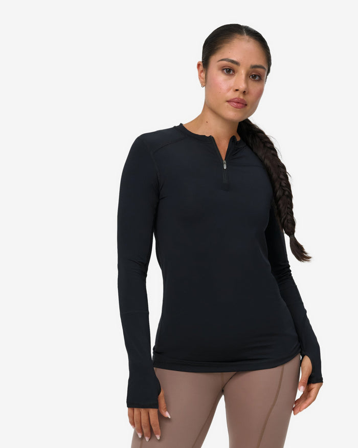 Woman wearing a black long-sleeve top and brown leggings on a white background