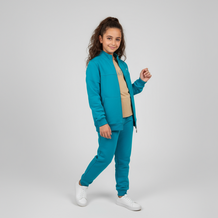 Child wearing a teal zip-up jacket with matching joggers, a beige t-shirt, and white sneakers.