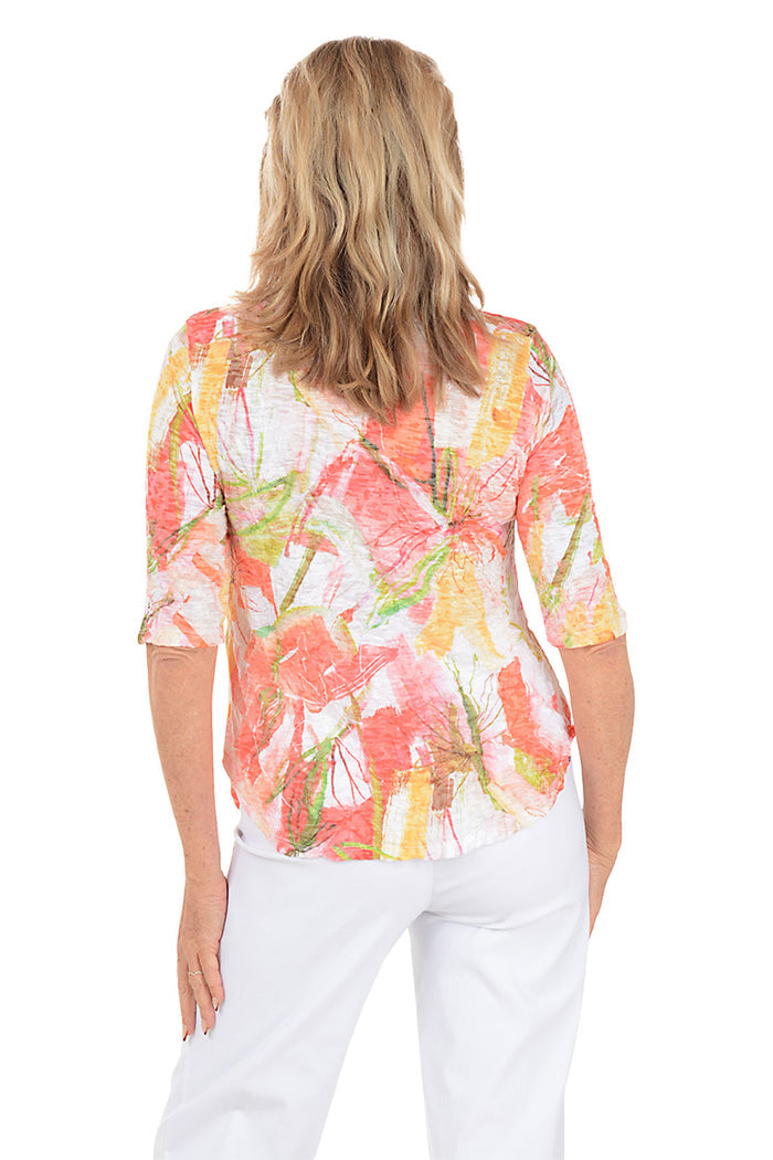 Woman wearing a colorful floral blouse and white pants on a white background. Back shot.